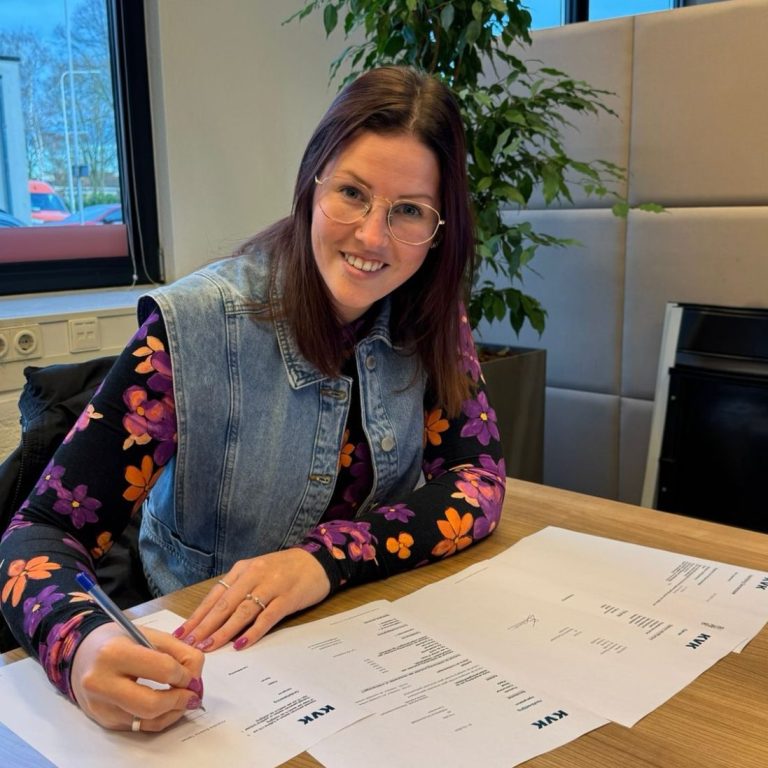 Eigen bedrijf met KVK Vrouw met een spijkerjack en bloemenblouse schrijft op papier aan een bureau.